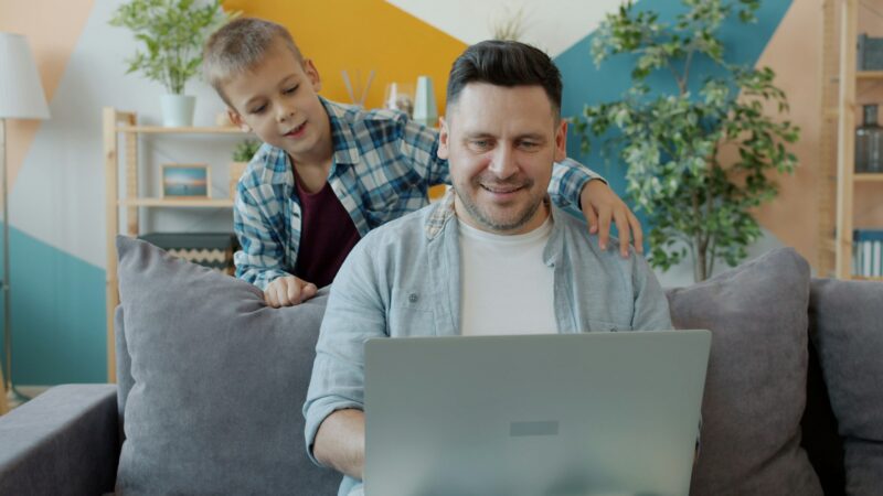 Father and son smiling at a laptop together at home